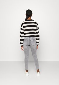 Černobílý pruhovaný nadměrně velký pletený svetr s dlouhými rukávy, kombinovaný s přiléhavými světle šedými džíny a bílými teniskami.