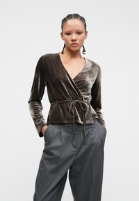 Top din catifea întunecată, cu mâneci lungi și un laț în talie, asortat cu pantaloni gri cu talie înaltă, prevăzuți cu pliuri.