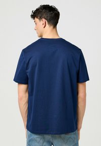 Laivastonsininen puuvillapaita, jossa on pyöreä kaula-aukko ja lyhyet hihat. Sujuva rakenne ja rento malli, nähtynä takaa, näkyvillä ompeluyksityiskohdat.