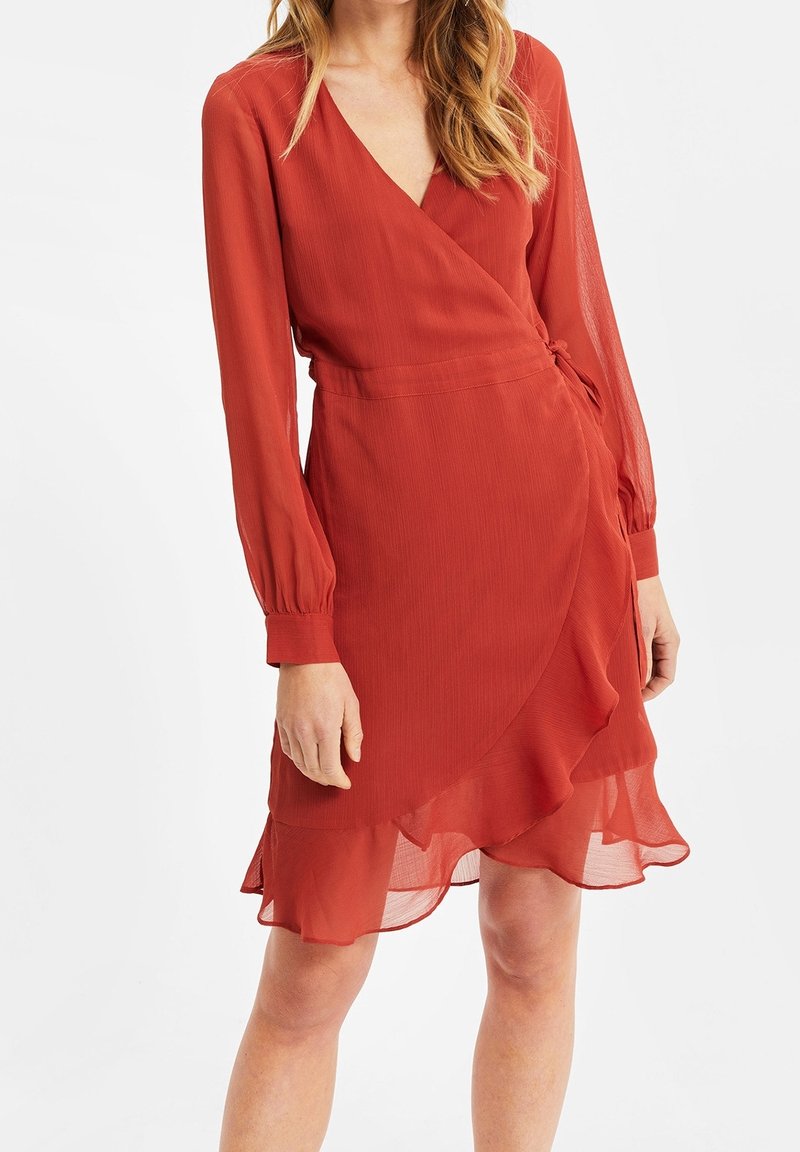 Robe rouge à manches longues, décolleté en V et ourlet à volants. Fabriquée en tissu léger avec une texture lisse et un détail ceinturé.