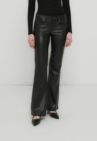 Pantalon évasé en similicuir noir avec une texture lisse, poches avant et détails en métal. Ajusté à la taille, large à l'ourlet.
