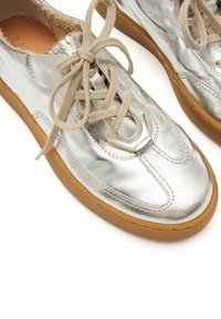 Sneaker in pizzo argento metallico con finitura liscia, punta rotonda e lacci beige, dotate di suola in gomma marrone.