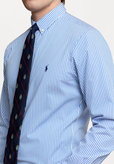 Camicia a righe blu chiaro e bianca con colletto button-down e cravatta blu navy con motivi di corone e scudi.
