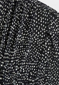 Tissu noir avec des plis verticaux serrés et des pois blancs irréguliers créant des sections texturées et froncées.