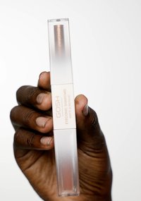 GOSH Eyeconic Shadows dans un tube transparent et givré avec une étiquette dorée, montrant une ombre métallique cuivrée à l'intérieur. Main tenant le produit.