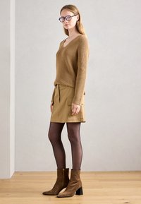 Brun ribbet genser med V-hals, kombinert med en beige skjørt med cargo-lommer og svarte strømper. Brune ankelstøvler med blokkhel.