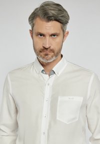 Jasno beżowa koszula zapinana na guziki z szarym kołnierzykiem, kieszonką na piersi i gładką teksturą, charakteryzująca się dopasowanym krojem i minimalistycznymi detalami.