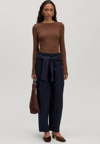 Bruine getailleerde top met lange mouwen, marineblauwe wijde broek met ribgebreide strikdetail ter hoogte van de taille, en bruine suède slingback schoenen, gecombineerd met een bruine tas.