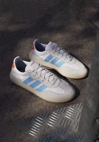 Vita och grå sneakers med ljusblå ränder, släta och texturerade paneler, rundad form, snörning och orange hälackent.