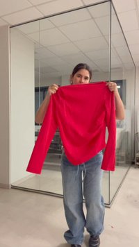 Personne tenant une chemise rouge vif à manches longues devant son torse dans un bureau moderne aux murs en verre.