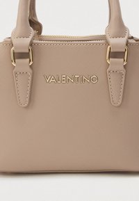 Beige handbag with a textured finish, gold hardware, double handles, and embossed "VALENTINO" logo on the front. Zipper closure on top.