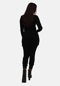Schwarzes, geripptes Longsleeve-Oberteil, kombiniert mit schwarzen, figurbetonten Cargo-Hosen. Das Model trägt schwarze Ankle-Boots mit einem stabilen Absatz.
