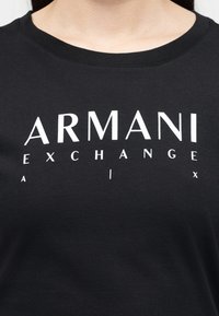 Μαύρο πουκάμισο με στρογγυλή λαιμόκοψη, με την επιγραφή "ARMANI EXCHANGE" σε μεγάλα λευκά γράμματα στο στήθος.