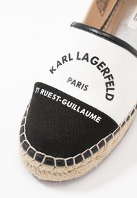 Espadrillas bianche in tela con pannello in cotone nero, caratterizzate da dettagli di cucitura e testo stampato: "KARL LAGERFELD PARIS 21 RUEST-GUILLAUME."