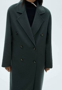 Donkergroene wollen jas met een dubbelgeknoopt ontwerp, grote afgeronde revers en decoratieve knopen. Heeft een tailored fit en een zachte textuur.
