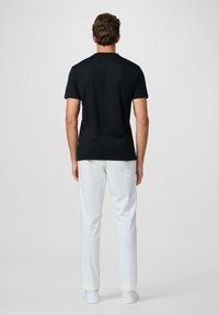 Camiseta de algodón negra de manga corta, combinada con pantalones blancos. La camiseta presenta un escote clásico y una textura suave.