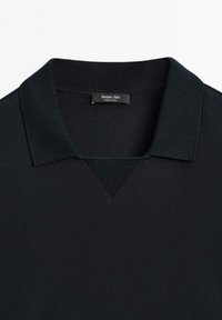 Černé polo tričko s texturovanou tkaninou, které má klasický límec a V-výstřih. Na štítku je napsáno "Massimo Dutti, VYROBENÉ V ČÍNĚ."