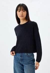 Marineblauer gerippter Strickpullover mit Rundhalsausschnitt und überschnittenen Schultern, kombiniert mit hellblauen gerade geschnittenen Jeans. Weicher Stoff und lässige Passform.