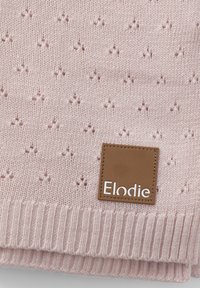Vaaleanpunainen neulottu huivi, jossa on teksturoitu kuvio pienistä tähdistä ja ruskea nahkatunnus, jossa brändin nimi "Elodie" on painettu valkoisella.