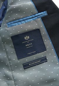 Interno di un blazer slim fit in navy e azzurro chiaro, con un motivo a pois, texture satinata e etichette per informazioni sul marchio e sulla cura.