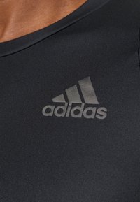 Camiseta atlética negra con un material suave y elástico. El logo de Adidas está sutilmente grabado en el pecho en un tono más oscuro de negro.