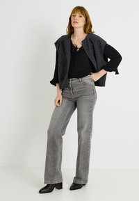 Chaleco de lana gris sobre una blusa negra con cordones en el frente, combinado con unos jeans grises de tiro alto y botines negros de tacón.