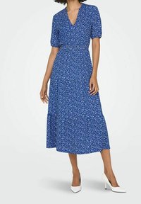 Sininen kukkakuosis midi-mekko lyhyillä puffi-hihoilla, V-pääntiellä, kapealla vyötäröllä ja levenevällä hameella; yhdistetty valkoisiin korkokenkiin.