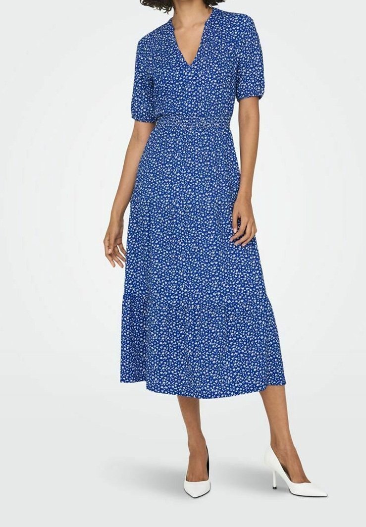 Sininen kukkakuosis midi-mekko lyhyillä puffi-hihoilla, V-pääntiellä, kapealla vyötäröllä ja levenevällä hameella; yhdistetty valkoisiin korkokenkiin.