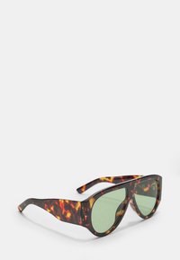Occhiali da sole tartarugati con lenti verdi, caratterizzati da una forma quadrata audace e montature spesse e strutturate. Accentati con motivi di colore vivaci.