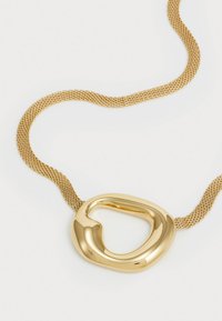 Collier pendentif en or avec une forme lisse et courbée et une ouverture centrale, attaché à une chaîne en mailles texturées en or.