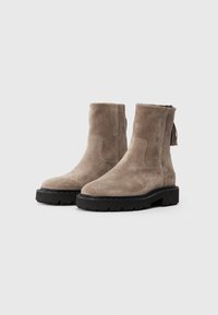 Bottines en daim gris clair avec une finition texturée, dotées d'une semelle en caoutchouc noir et d'un détail de gland à l'arrière.
