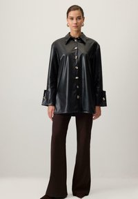 Sort faux læder skjorte med spids krave, seks sølvfarvede knapper og brede manchetter. Matchet med mørkebrune flagrende bukser.