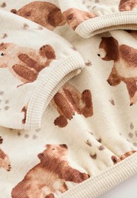 Tissu en crème doux avec des illustrations de teddy bears bruns et des bords côtelés, montrant des détails en gros plan de la texture du textile et des motifs de bears.