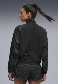 Μαύρο αδιάβροχο με γιακά ψηλό, διακοσμημένο με υφασμάτινα μανίκια με ανάγλυφο σχέδιο. Ελαφρύ ύφασμα, με ελαστική μέση, συνδυασμένο με αντίστοιχα σορτς.