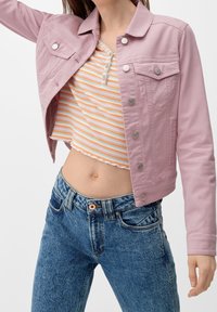 Chaqueta de mezclilla rosa claro con bolsillos delanteros y botones plateados, combinada con una camiseta de rayas y jeans de tiro alto azules.