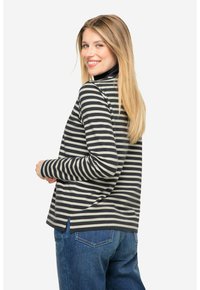 Sort-hvid stribet langærmet top med høj halsudskæring, afslappet pasform og sideslids, parret med mørkeblå jeans.