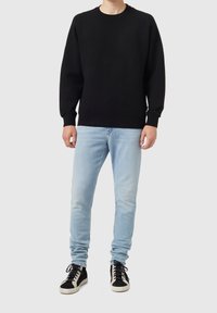 Sudadera negra con cuello redondo y mangas largas, combinada con vaqueros ajustados de color azul claro y zapatillas negras con suelas y cordones blancos.