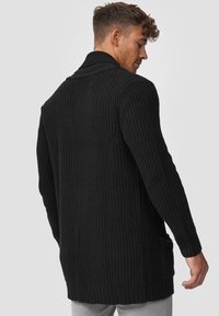Cárdigan negro de punto con mangas largas, cuello de chal y bolsillos laterales. Presenta una tela texturizada y dobladillos acanalados.
