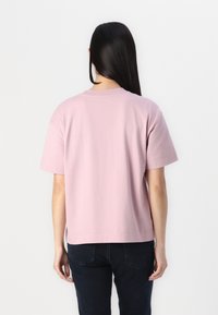 Koszulka z krótkim rękawem, okrągłym dekoltem, w jasnoróżowym bawełnianym materiale, o luźnym kroju i minimalnym haftowanym wykończeniu na dolnym brzegu.