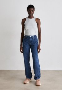 Gray sleeveless top paired with high-waisted blue jeans. Model wears light pink sneakers. Simple design, fitted top, and straight-leg jeans.