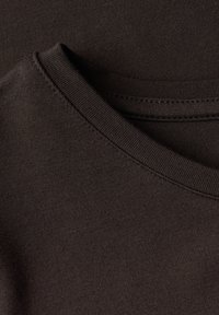 Tummanruskea puuvillakangas, jossa on sileä pinta, esittelee pyöreän pääntien ja siistin, viimeistellyn reunan kauluksessa.