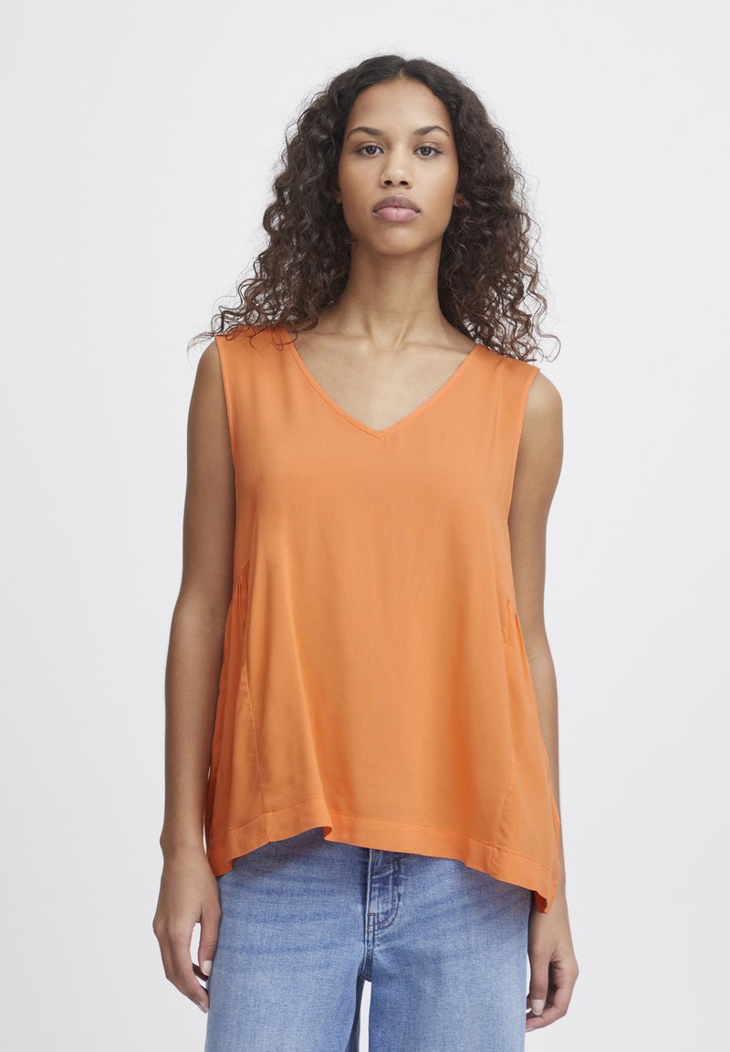 Sleeveless orange top with a V-neck design, loose fit, soft texture, and side pockets. Paired with light blue jeans.