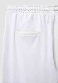 Weiße Stretch-Hosen mit einem Nahaufnahme eines Gesäßtasche, die einen Klappenverschluss und strukturierten Stoff zeigt.