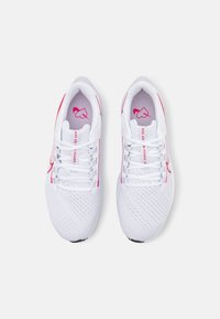 Une paire de chaussures de course Nike blanches avec des accents roses, des parties en maille et des lacets, vues de dessus sur un fond blanc.