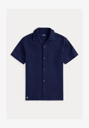 Laivastonsininen lyhythihainen paita teksturoidusta kankaasta, jossa on napitettu edusta, kaksi rintataskua ja pieni logokoriste. Ruskeat napit.