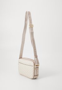 Bolso cruzado en crema con un patrón entrelazado de "MK", herrajes dorados y una correa de tela suave que presenta el logo "MICHAEL KORS".