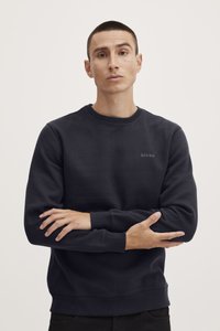 Sudadera de un azul marino oscuro con cuello redondo, puños acanalados y un pequeño logo en el pecho. Tejido suave con una textura lisa, corte relajado.