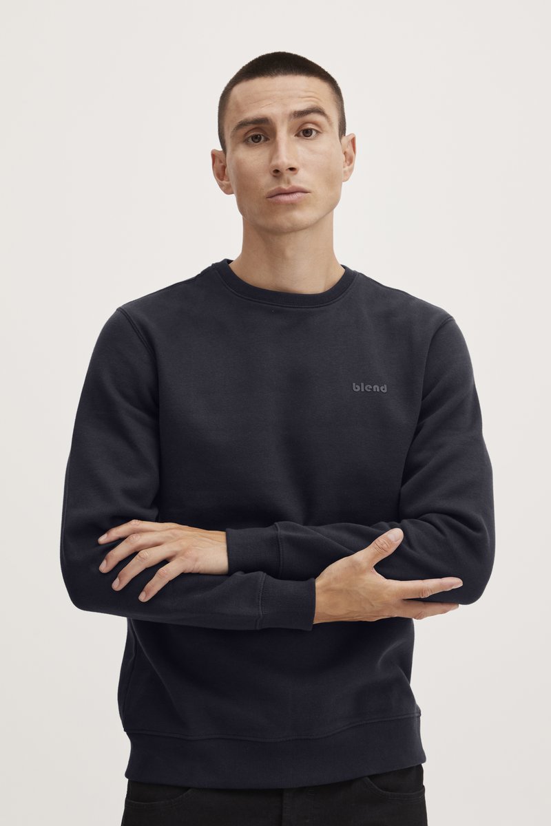 Sudadera de un azul marino oscuro con cuello redondo, puños acanalados y un pequeño logo en el pecho. Tejido suave con una textura lisa, corte relajado.