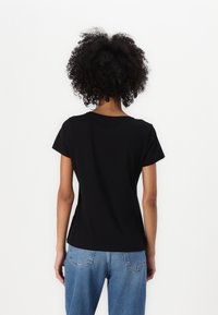 Czarna bawełniana koszulka z krótkim rękawem, okrągłym dekoltem i dopasowanym krojem. Noszona z jasnoniebieskimi dżinsami. Gładki, bezszwowy widok z tyłu.