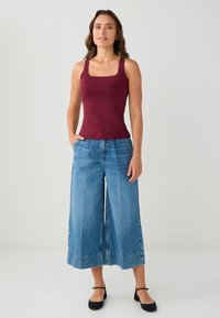 Bordeaux tanktop met vierkante halslijn, gecombineerd met wijde, lichtblauwe denim culottes met een rafelrand. Model draagt zwarte ballerina's.